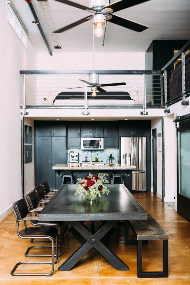 Массивный и грубый обеденный стол с металлической столешницей, бетонный пол, конструктивно-шинные светильники создают тематическую атмосферу в квартире индустриального стиля