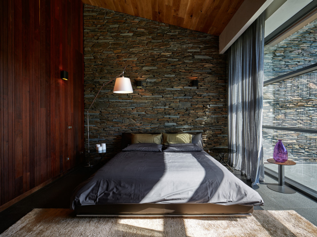 Спальня в стиле лофт с темно-коричневым ламинатом на одной стене и декоративным камнем на другой